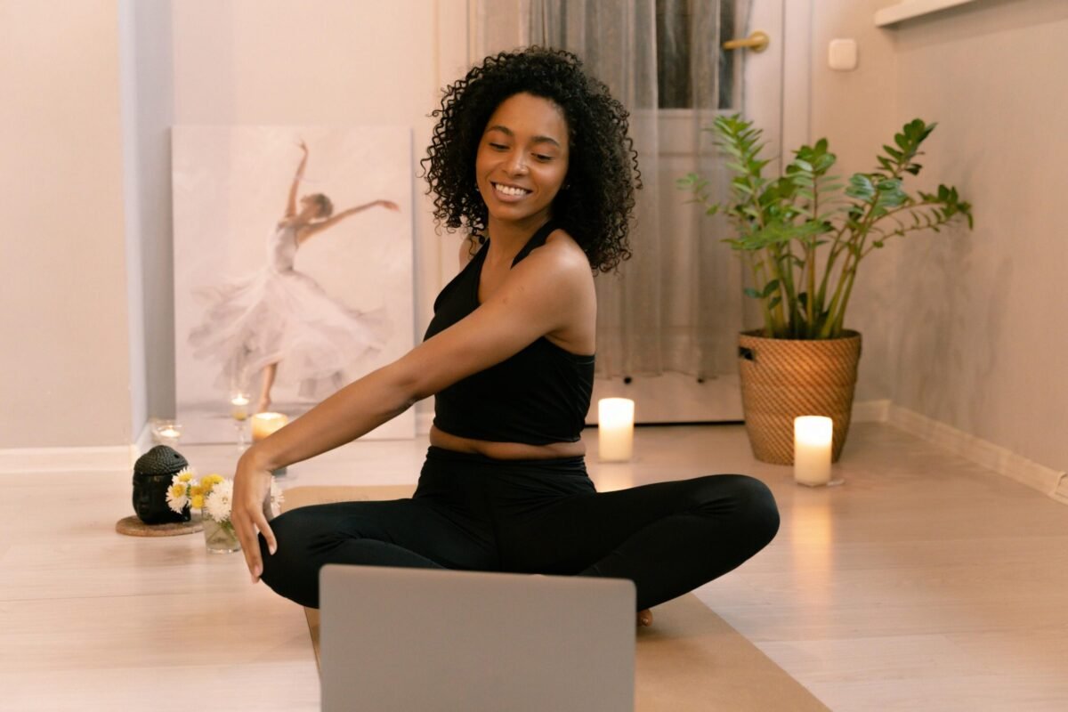 African American woman practicing yoga indoors with laptop and candles.