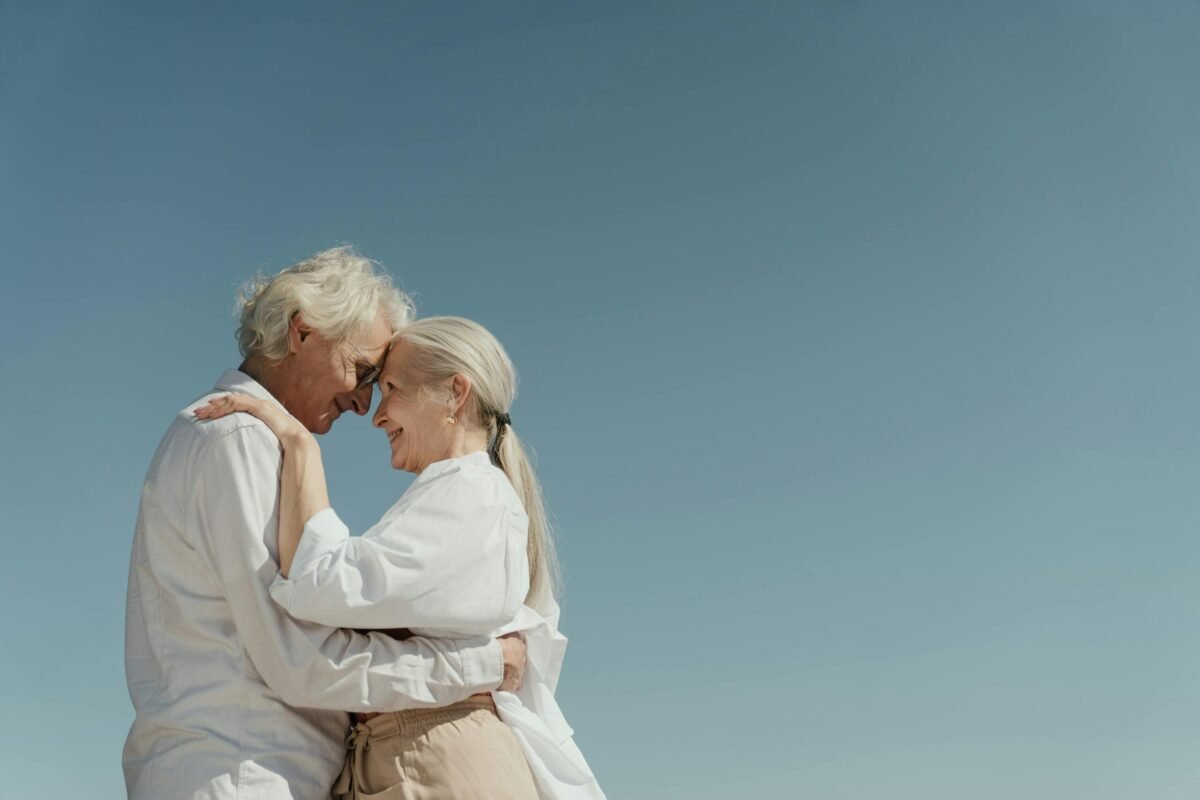 Senior couple embracing outdoors, depicting love and happiness against a clear blue sky.