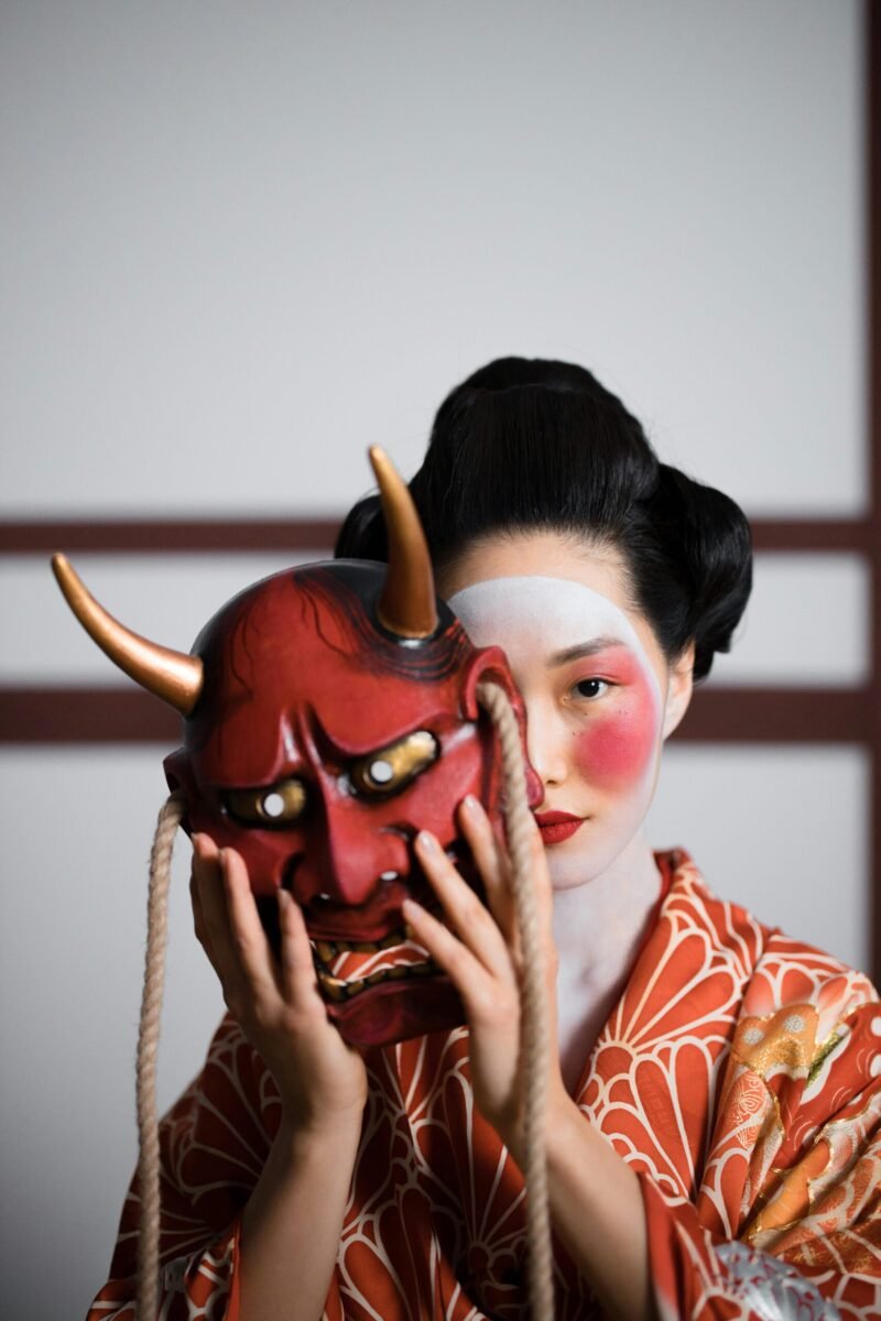 Portrait of a Japanese woman in traditional kimono holding a Hannya mask.