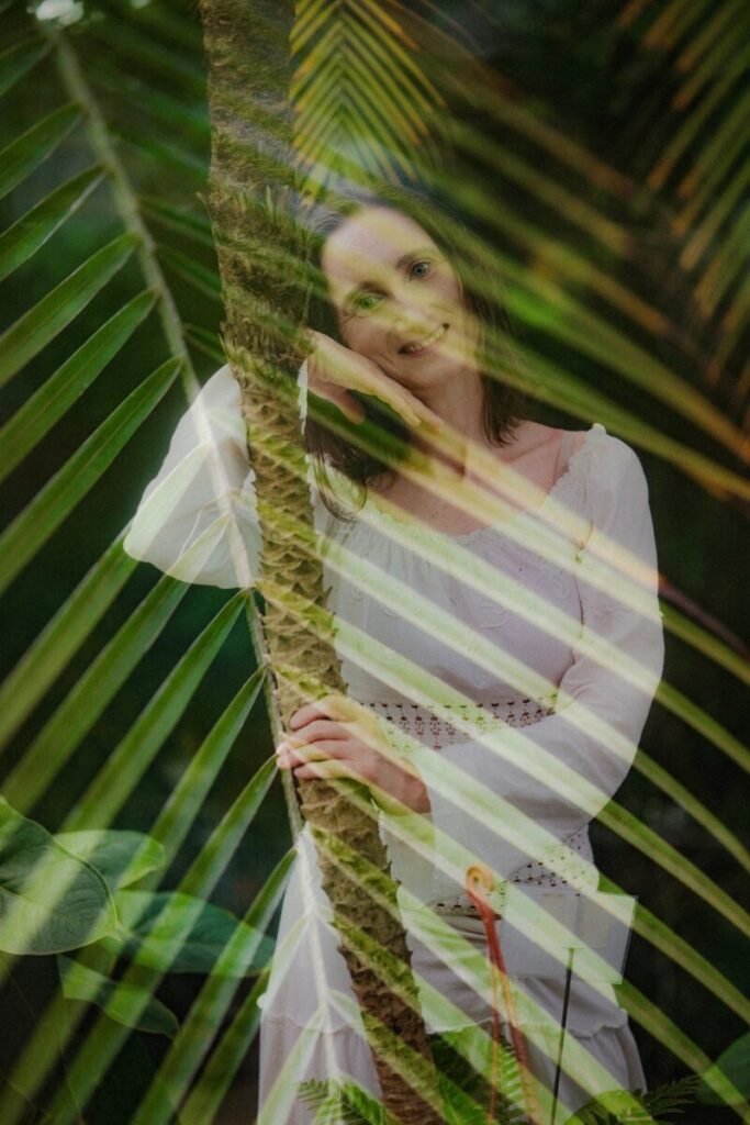 Aviva Method–supportive guided relaxation and hypnotherapy image showing a calm, smiling practitioner in white behind leaves, symbolizing an invitation to relax, release stress, and set up emotional balance.