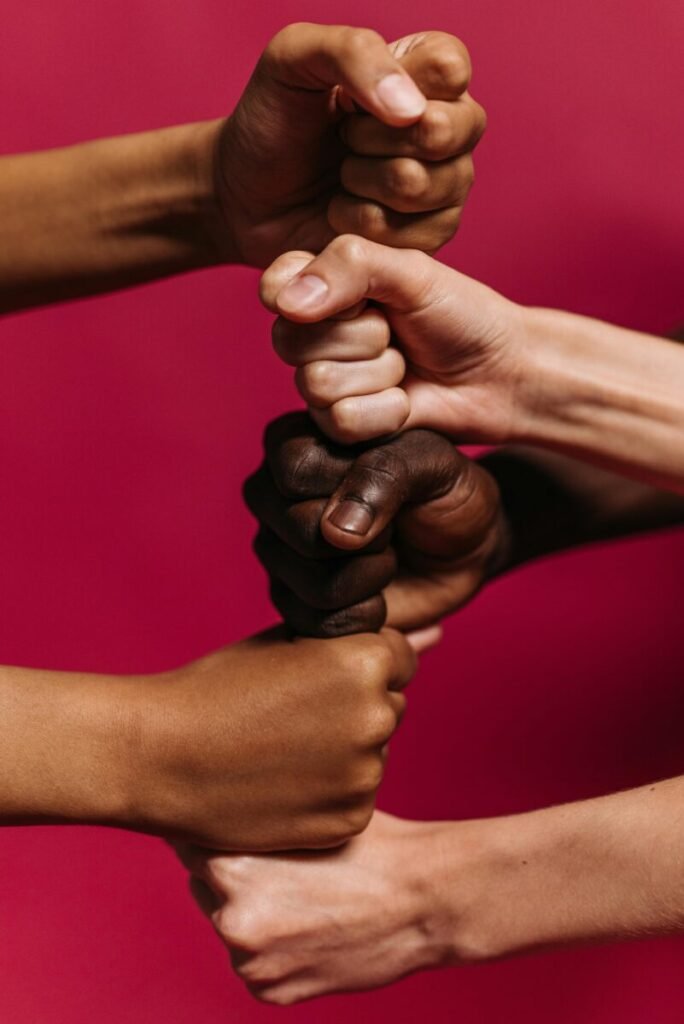 Close-up of diverse hands clenched together against a vibrant pink background symbolizing unity and strength.